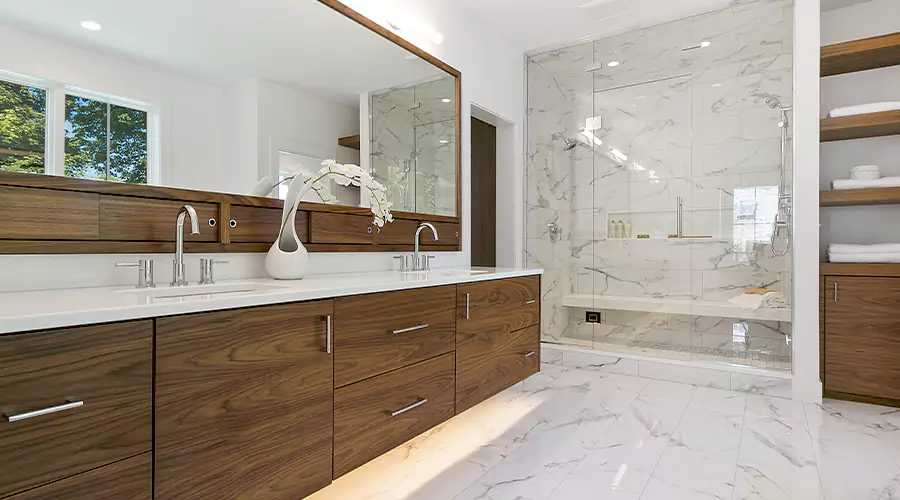 Luxury white bathroom renovation featuring large marble tiles, gold fixtures, and a frameless glass shower enclosure